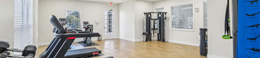 A gym with a variety of equipment including treadmills, weights, and a bench.