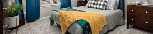 A bedroom with a bed, nightstand, and window with blue curtains.