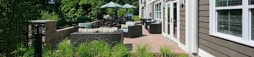 A patio area with a table and chairs is surrounded by a grassy area and a building.