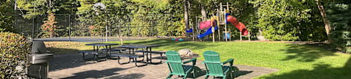 A playground with a slide and picnic tables surrounded by trees.
