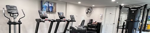 A spacious gym with treadmills, elliptical machines, and a weight rack.