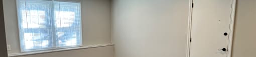 A room with a white door and a window with blinds.