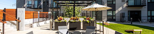 A patio with chairs and a table with a planter in front of a building.