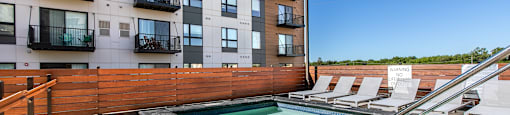 A pool area with a hot tub and lounge chairs in front of a multi-story apartment building.