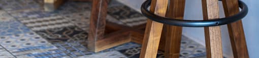 Three wooden stools with grey cushions are lined up on a tiled floor.