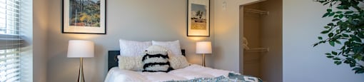 A bedroom with a bed, two lamps, and a painting on the wall.