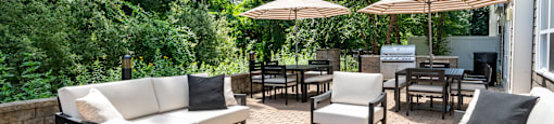 A patio with white couches, chairs, and umbrellas surrounded by trees.
