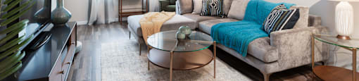 A living room with a grey couch, a glass table, and a painting on the wall.