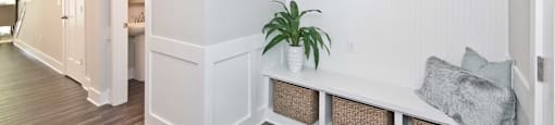 A white bench with baskets underneath is in a room with wood flooring.