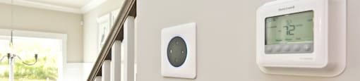A wall-mounted thermostat and a wall-mounted smoke detector are installed on a wall.