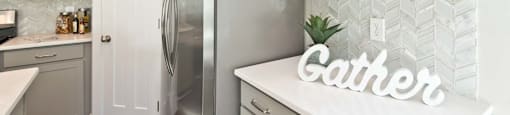 A kitchen with a refrigerator and a countertop with a sign that says "Gather".