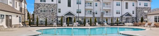 Apartments in Ashland City - Ashland Farms - Expansive Swimming Pool Area with Sundeck and Ample Lounge Chair Seating with Apartment Building in the Background.