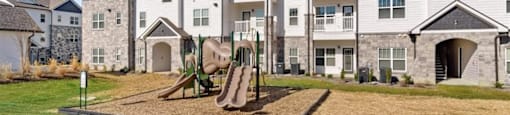 Apartments for Rent in Ashland City, TN - Ashland Farms - Playground with Wood Chips-Covered Ground, Slide Set, Surrounding Grass Lawn, and Apartment Building in the Background