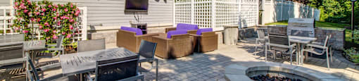 Fire pit with four person tables and grilling station with gas grill. Mounted outdoor TV with additional soft seating positioned in front.