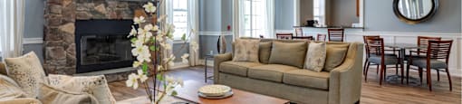 Angled view of furnished clubhouse with couches situated in front of fireplace and two tables with four chairs in background at Summit Place apartments in Methuen, MA.