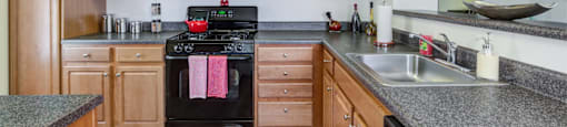Kitchen with hardwood-style flooring, honey upper and lower cabinets with ample countertop space and black oven with mounted microwave above at Summit Place apartments in Methuen, MA.