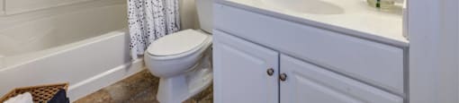 Bright white bathroom with white vanity and built-in linen closet. Oversized mirror hung above vanity with toilet and shower to the left at Summit Place apartments in Methuen, MA.