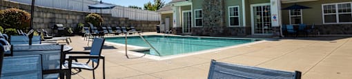 a swimming pool in front of a house with chairs and umbrellas