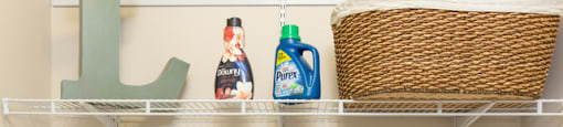 Two white washing machines are in a laundry room with a shelf above them.