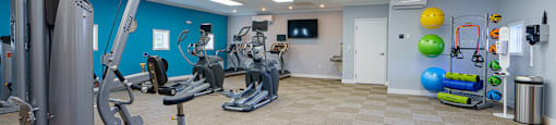A gym with a variety of equipment and a TV on the wall.