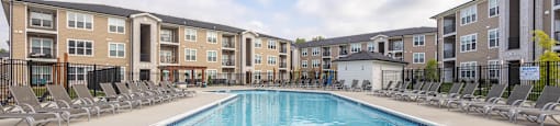 A swimming pool with blue lounge chairs and apartment buildings in the background.