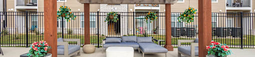 A wooden pergola is in the middle of a patio with cushioned seating and potted plants.