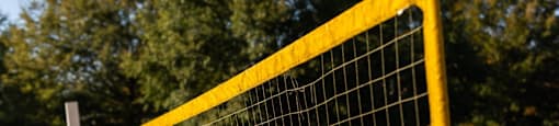 A yellow volleyball net is set up on a sandy area.