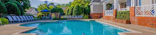 A large outdoor swimming pool surrounded by a brick wall and lounge chairs.