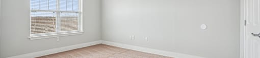 A room with a carpeted floor and a window with blinds.