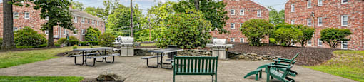 A green lawn with a picnic table and chairs in front of a brick building.
