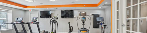 A gym with orange walls and a variety of exercise equipment.