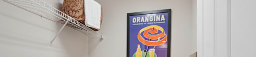 A laundry room with a washer and dryer, a basket on the shelf, and a poster on the wall.
