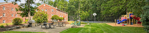 A playground with a slide and a picnic table is surrounded by trees.