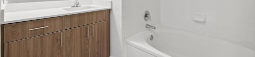 A white bathroom with a wooden vanity and a white bathtub.
