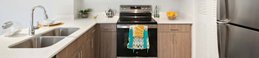 A modern kitchen with a stainless steel refrigerator, a stove with a towel on it, and a sink with a bowl on it.