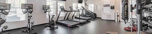 A gym with a variety of exercise equipment including treadmills, stationary bikes, and weight machines.