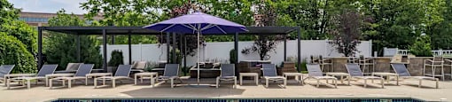 A pool with a blue umbrella and chairs around it.