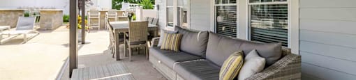A patio with a grey couch and a table with chairs.