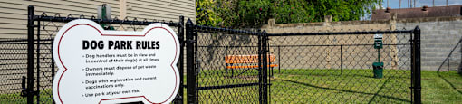 a dog park rules sign on a fence in front of a house