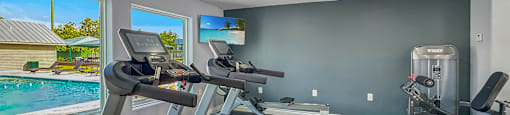 A Spin bike is in a room with a view of a pool and a house.
