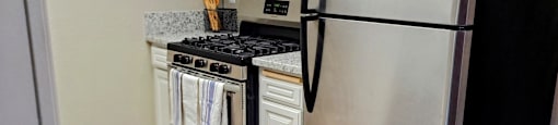 A black refrigerator stands in a kitchen with a stove and microwave in the background.
