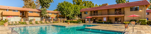 A swimming pool in front of a building with a red umbrella.