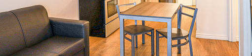 A black couch sits in a kitchen with a table and chairs.