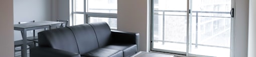A black leather sofa sits in a living room with a coffee table and a dining table.