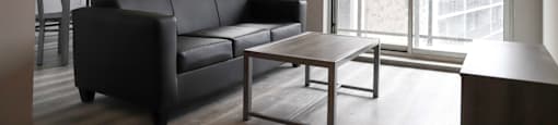A black leather couch sits in a living room with a coffee table in front of it.