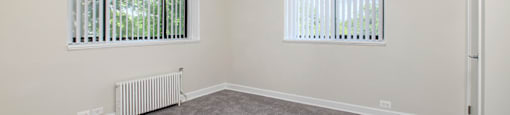 A room with a ceiling fan and two windows with blinds.
