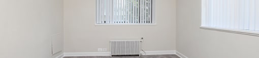 A room with a grey carpet, a ceiling fan, and a radiator.