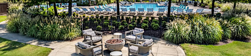 A round patio area with a fire pit surrounded by chairs and trees.