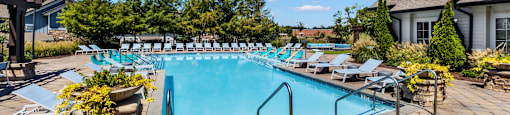 A large outdoor swimming pool surrounded by lounge chairs and potted plants.