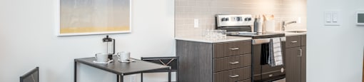 Two-Bedroom Apartments in Eugene, OR - Crosswood - Kitchen with Wood Plank Flooring, Table and Chairs, Quartz Countertops with Tile Backsplash, Wood-Tone Cabinetry, and Stainless-Steel Appliances.